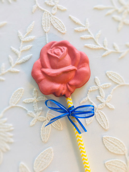 QUEST XO Rose Lolly: on a floral background, a lolly with a yellow stick, blue ribbon, and a rose lolly coloured red.
