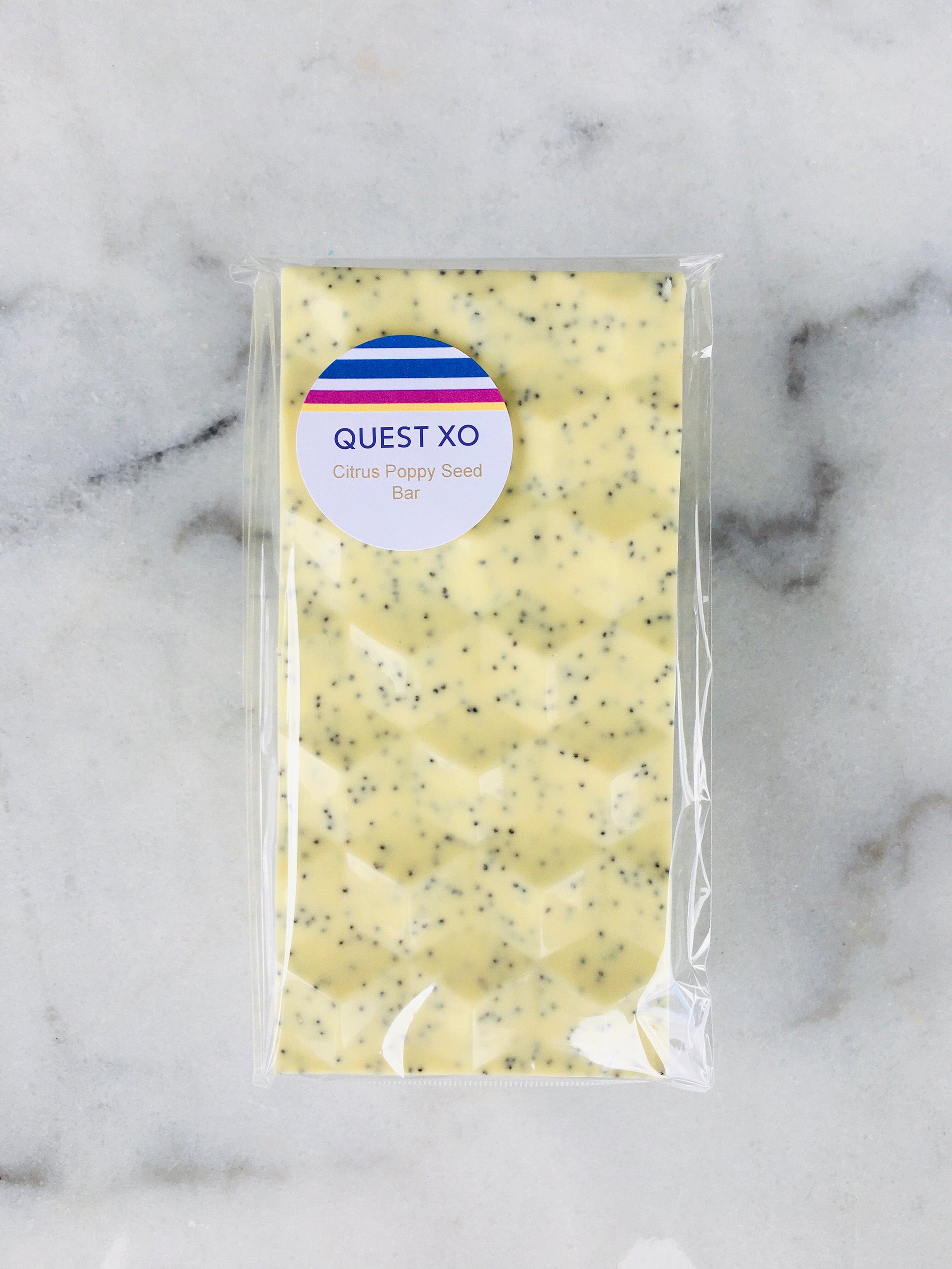 QUEST XO Citrus Poppy Seed Bar: White chocolate bar packed in transparent packing with QUEST XO logo placed on a marble background.