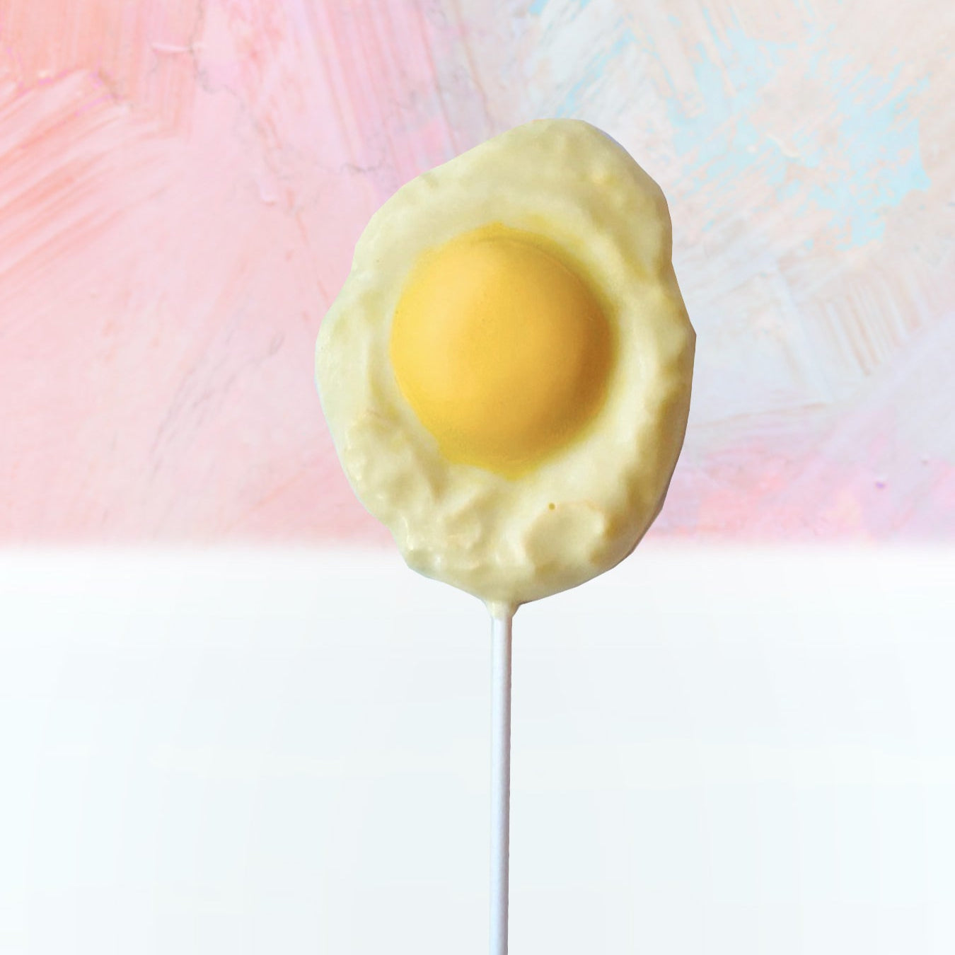 QUEST XO Egg Lolly: Sunny side up shaped lollipop with white stick placed on a pink and white background.