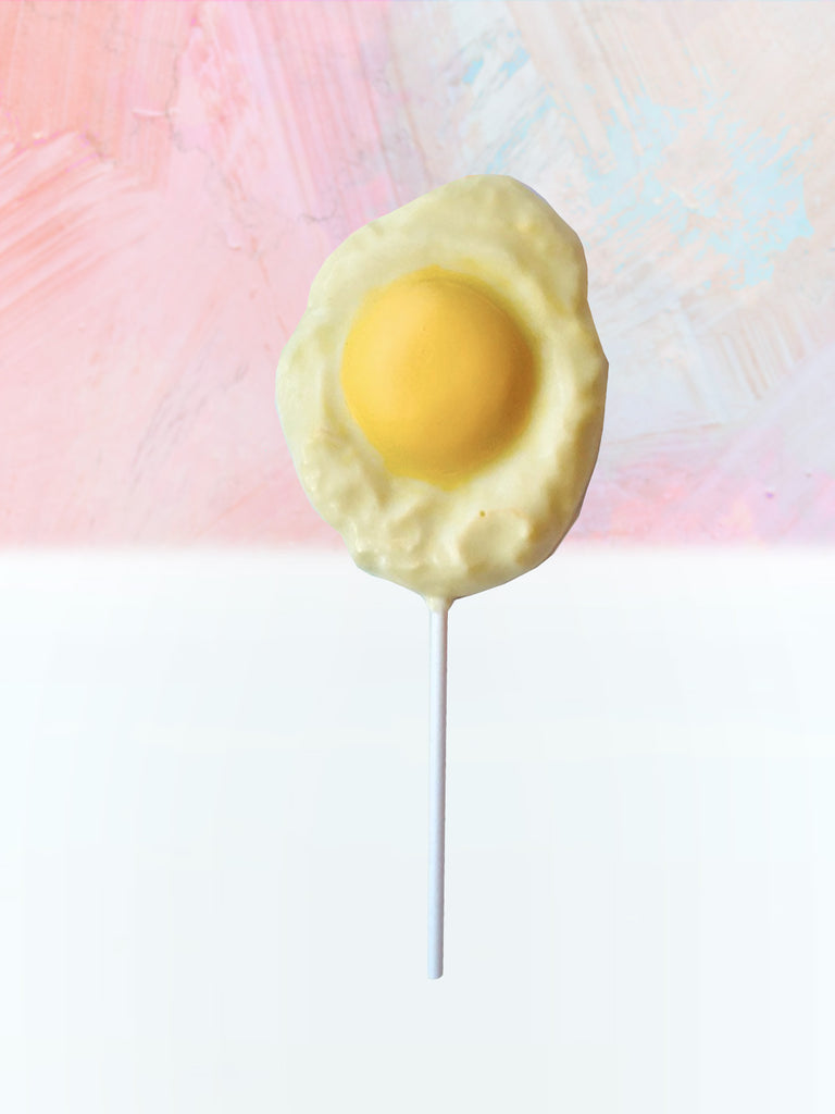 QUEST XO Egg Lolly: Sunny side up shaped lollipop with white stick placed on a pink and white background.