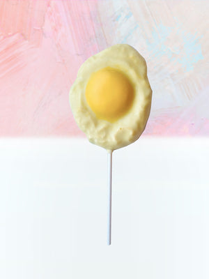 Open image in slideshow, QUEST XO Egg Lolly: Sunny side up shaped lollipop with white stick placed on a pink and white background.
